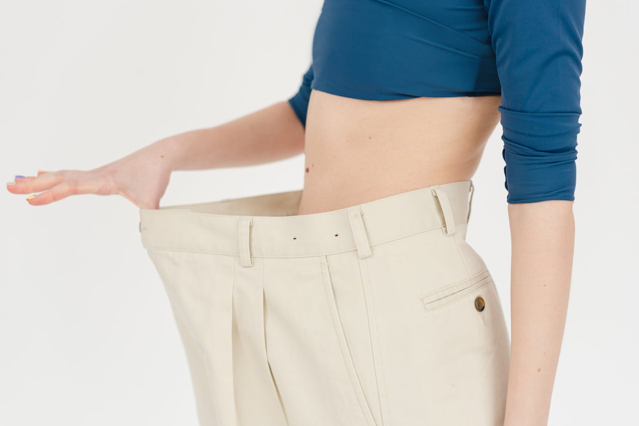 get-in-touch A woman demonstrates significant weight loss by wearing oversized pants indoors.